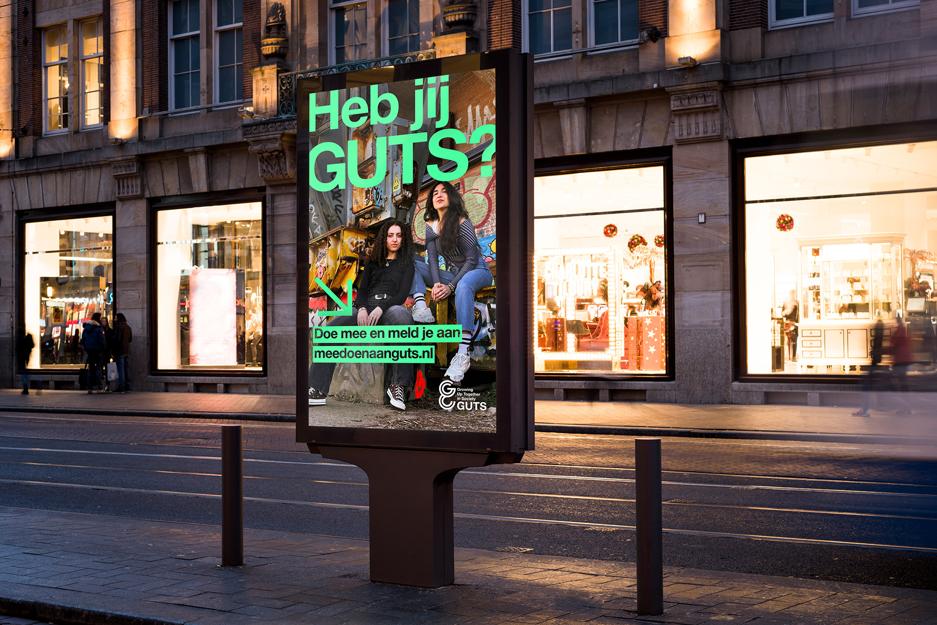 Een billboard met event branding toont twee jonge vrouwen zittend op een trapje, één met krullend haar en één met steil haar. Vetgedrukte groene tekst vraagt "Heb jij GUTS?" met een groene pijl naar "Doe mee en meld je aan meedoenaan guts.nl.".